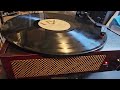 Music by ELO titled FIRST MOVEMENT (JUMPIN BLIZ) from 1971 played on an actual record player.